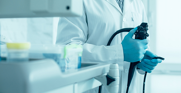 a doctor wearing a white lab coat and blue latex gloves holding endoscopy equipment